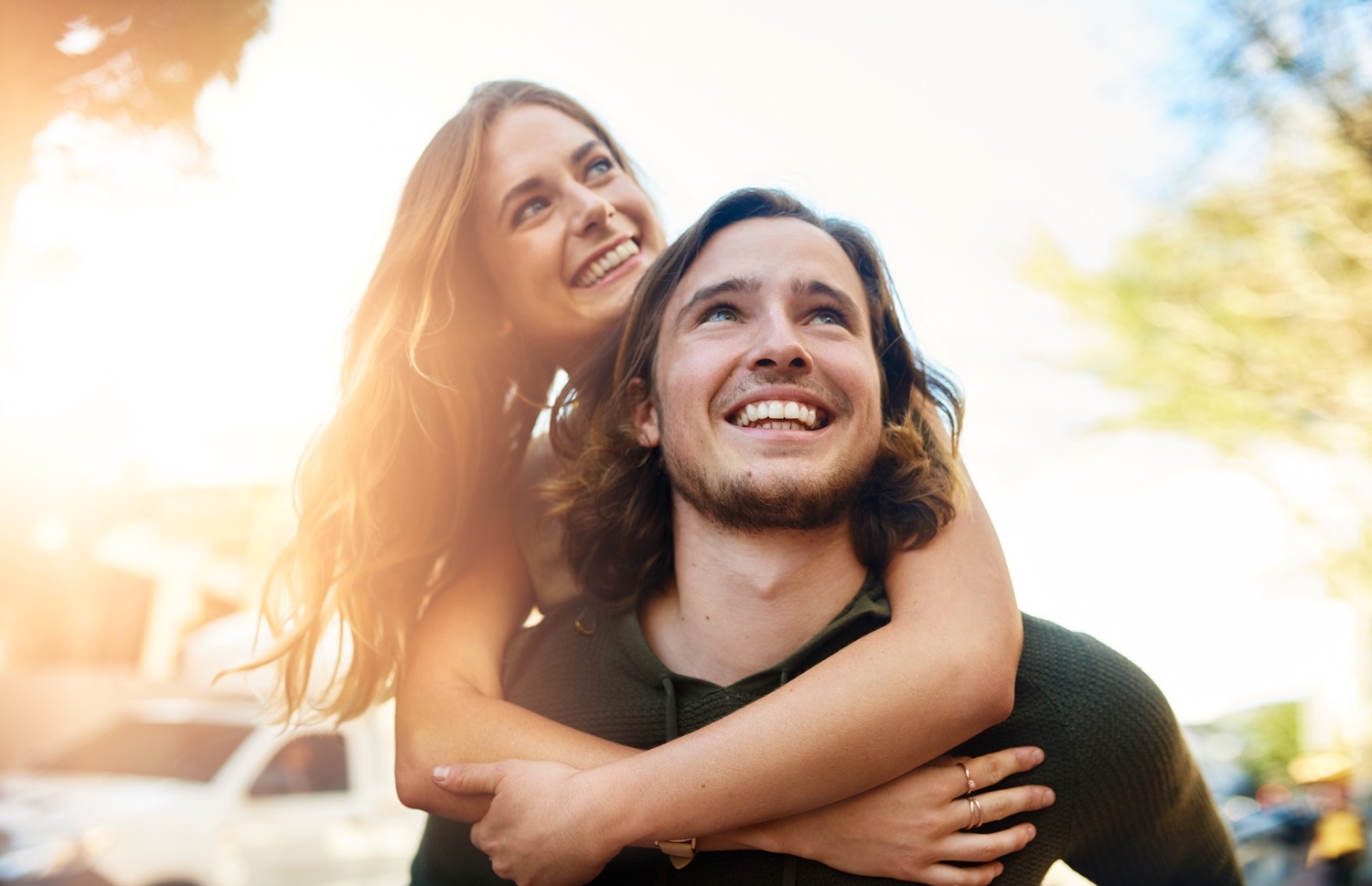 Young couple smiling outdoors in bright sunlight, representing cosmetic dental care in San Diego for the La Mesa community